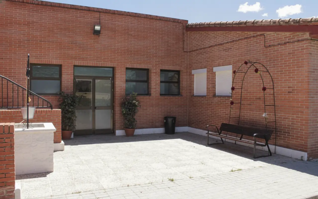 Patio de entrada del albergue con bancos, plantas y pozo de piedra