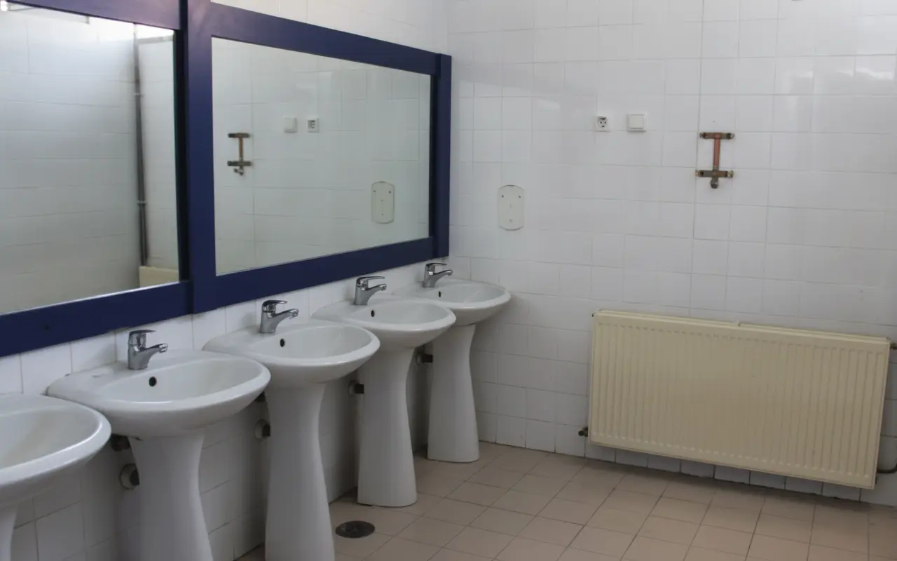 Fila de lavabos con espejos en un baño alicatado de blanco