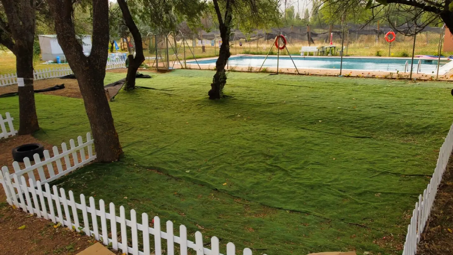 Pradera de césped con árboles y valla blanca junto a la piscina